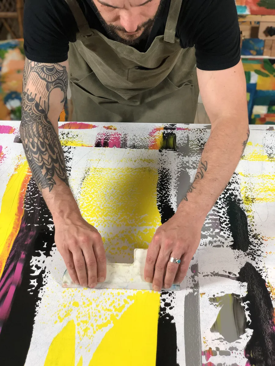 Pulling paint across a canvas with a scraper.